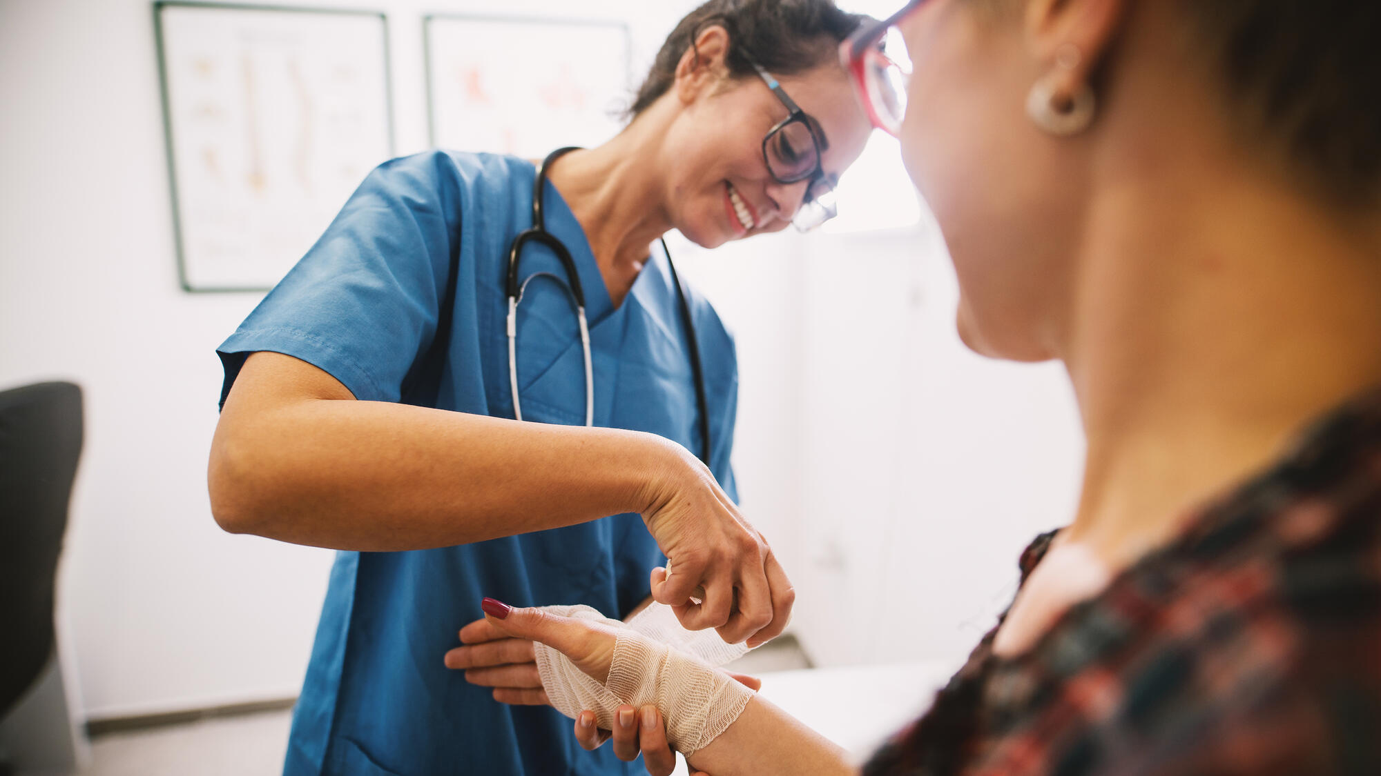 Professional nurse at the hospital bandaging the hand with a medical bandage for a woman patient.