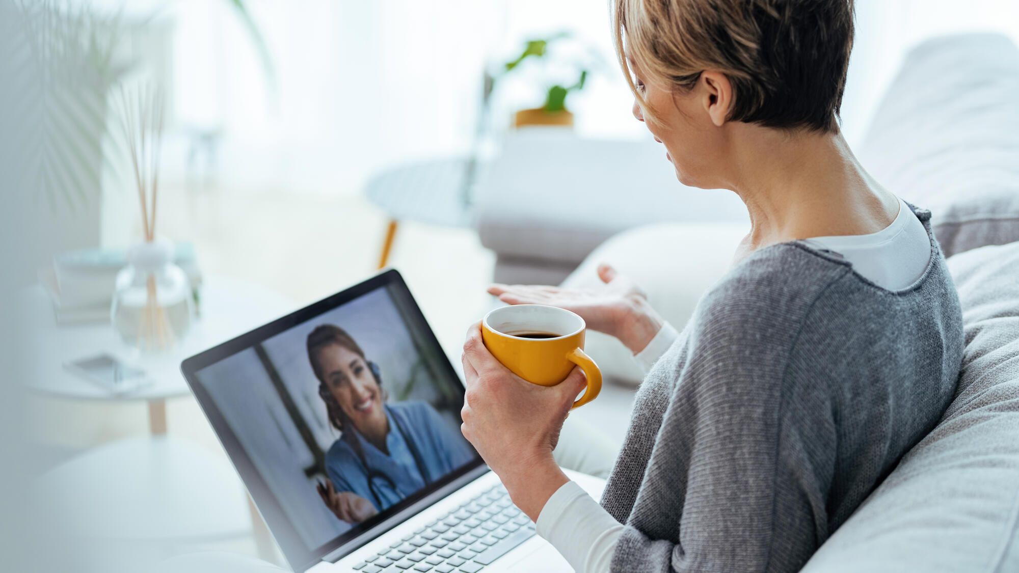 Woman on the couch, drinking coffee and speaking with her provider virtually