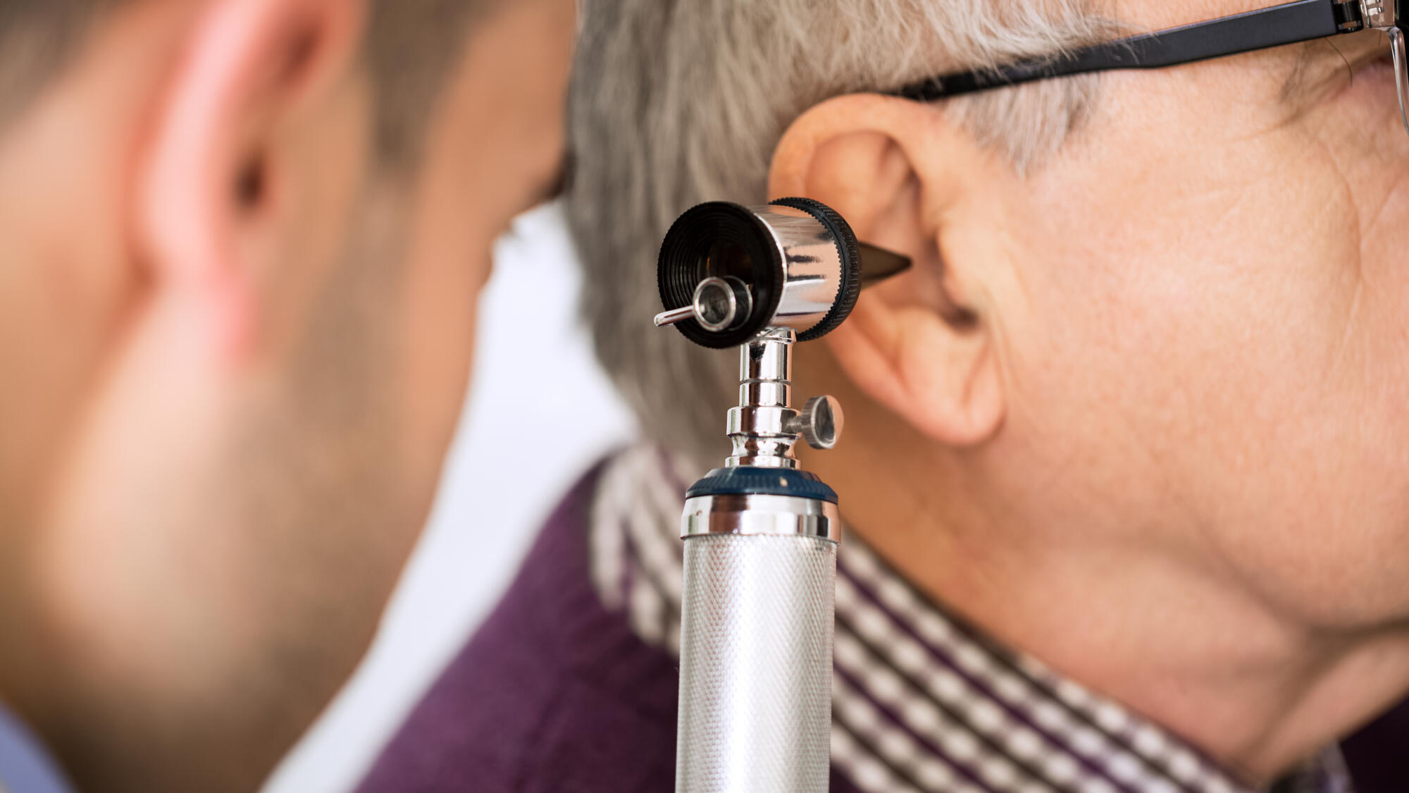 Doctor using otoscope to check a senior's ear
