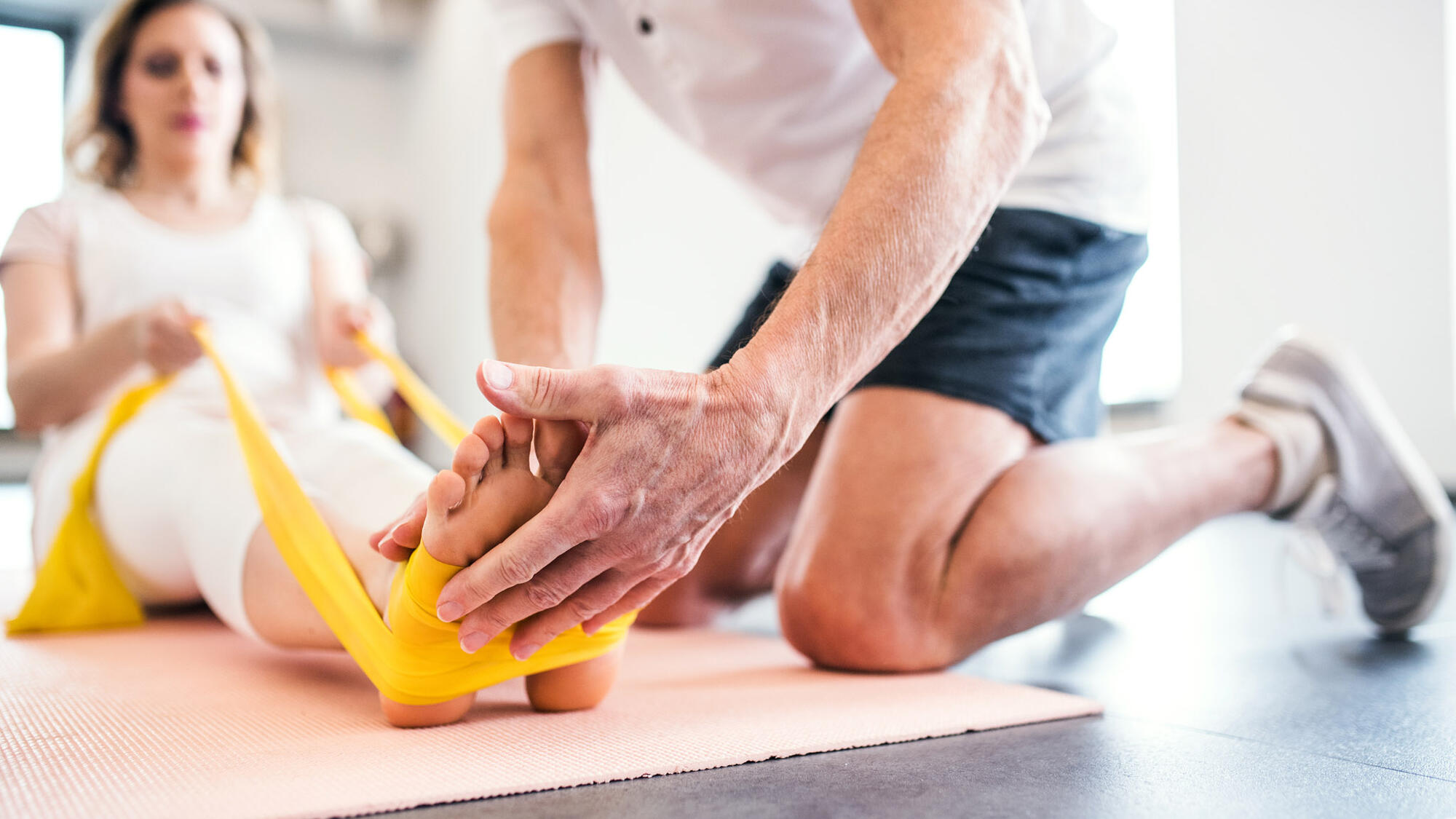Trainer helping a woman stretch with exercise bands